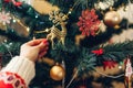 Woman decorating Christmas tree with golden deer ornament at home, wearing winter sweater. Preparing to New year. Royalty Free Stock Photo