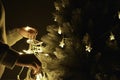 Woman decorating christmas tree with lights at home, wearing winter sweater