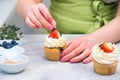 Woman decorating cupcakes in kitchen. Professional confectioner decorating top of cupcake with strawberry. Homemade pastry Royalty Free Stock Photo