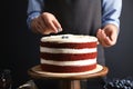 Woman decorating delicious homemade red velvet cake with blueberries