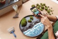 Woman decorator making photo of green ikebana on tray with epoxy resin in florist workshop