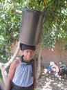Woman delicately balancing a bucket of water on her head.