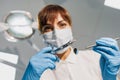 Woman dentist in blue face mask and gloves examine teeth with syringe and mirror. View from patient seat to doctor Royalty Free Stock Photo