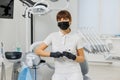 Woman dentist in white uniform, black face mask and gloves sitting in stomatology cabinet among modern dental equipment
