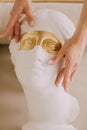 Woman cosmetologist shows massage technique on a statue with golden eyes.