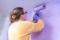Woman designer paints wall with a roller in color very peri renovates cozy home