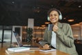 A woman at a desk wearing headphones smiles while drinking coffee and working in nice modern coworking office Royalty Free Stock Photo