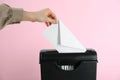 Woman destroying envelope with shredder on pink background, closeup