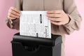 Woman destroying sheet of paper with shredder on pink background, closeup