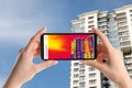 Woman detecting heat loss in building using thermal viewer on smartphone. Energy efficiency