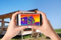 Woman detecting heat loss in house using thermal viewer on smartphone. Energy efficiency