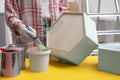 Woman dipping brush into bucket of green paint at yellow wooden table indoors, closeup Royalty Free Stock Photo