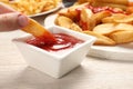 Woman dipping delicious baked potato wedge into bowl with ketchup at wooden table, closeup