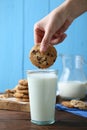 Woman dipping delicious chocolate chip cookie into glass of milk at wooden table, closeup Royalty Free Stock Photo