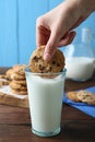 Woman dipping delicious chocolate chip cookie into glass of milk at wooden table, closeup Royalty Free Stock Photo