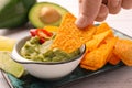 Woman dipping delicious nachos chip into guacamole at white wooden table, closeup