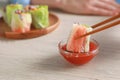 Woman dipping delicious spring roll wrapped in rice paper into sauce at white wooden table, closeup