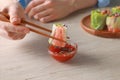 Woman dipping delicious spring roll wrapped in rice paper into sauce at white wooden table, closeup Royalty Free Stock Photo
