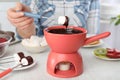 Woman dipping marshmallow into pot with chocolate fondue at table