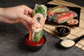Woman dipping roll wrapped in rice paper into sauce at grey table, closeup Royalty Free Stock Photo