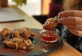 Woman dipping tasty BBQ wing into sauce at table