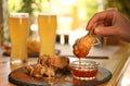Woman dipping tasty BBQ wing into sauce at table