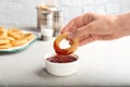 Woman dipping tasty onion ring into bowl with ketchup