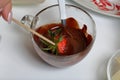 A woman dips strawberries in black melted chocolate. Cooking strawberries glazed in chocolate