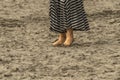 Woman with dirty feet and toes dug into the sand on the beach with longish dress - bottom one third of body - close-up and