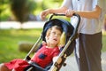 Woman with disabled girl in a wheelchair walking in the Park summer. Child cerebral palsy. Disability. Means of rehabilitation.