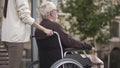 Woman with disabled grandfather in wheelchair walking in park, volunteering