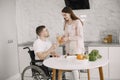 Wife encourage disabled husband sitting in wheelchair at kitchen table Royalty Free Stock Photo