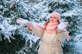 A woman with a displeased sad face stands by the snowy trees in the winter foreste. Decorating trees with toys in nature with