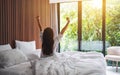 A woman do stretching after waking up in the morning , looking at a beautiful nature view outside bedroom