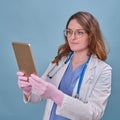 Woman doctor with a digital tablet Apple iPad in a white uniform on a blue studio background - Moscow, Russia, August 12, 2021