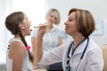 Woman doctor examining little girl mouth at office. Doctor at hospital checking the sore throat of a young patient