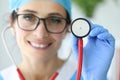 Woman doctor with glasses smiling and holding stethoscope.