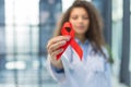 Woman doctor holding a red ribbon in her hand an international day of protecting people from cancer by symbol of