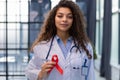 Woman doctor holding a red ribbon in her hand an international day of protecting people from cancer by symbol of