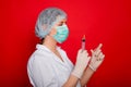 Woman doctor in medical clothes holds a syringe and an ampoule in her hands. Studio photo on a red background. Royalty Free Stock Photo