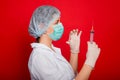 Woman doctor in medical clothes holds a syringe and an ampoule in her hands. Studio photo on a red background. Royalty Free Stock Photo