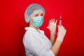 Woman doctor in medical clothes holds a syringe and an ampoule in her hands. Studio photo on a red background. Royalty Free Stock Photo