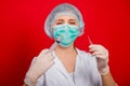 Woman doctor in medical clothes holds a syringe and an ampoule in her hands. Studio photo on a red background. Royalty Free Stock Photo