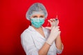 Woman doctor in medical clothes holds a syringe and an ampoule in her hands. Studio photo on a red background. Royalty Free Stock Photo