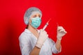 Woman doctor in medical clothes holds a syringe and an ampoule in her hands. Studio photo on a red background. Royalty Free Stock Photo