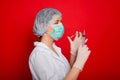 Woman doctor in medical clothes holds a syringe and an ampoule in her hands. Studio photo on a red background. Royalty Free Stock Photo