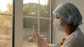 Woman doctor in medical mask puts on rubber gloves on the background of the window