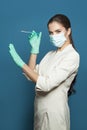 Woman doctor or nurse in professional medical uniform and protective face mask holding syringe on blue background, medicine, Royalty Free Stock Photo