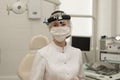 woman-doctor-otolaryngologist in a modern office ENT of the hospital, looks into the camera in a white coat and a mask Royalty Free Stock Photo