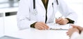 Woman doctor and patient sitting and talking at medical examination at hospital office, close-up. Therapist filling up